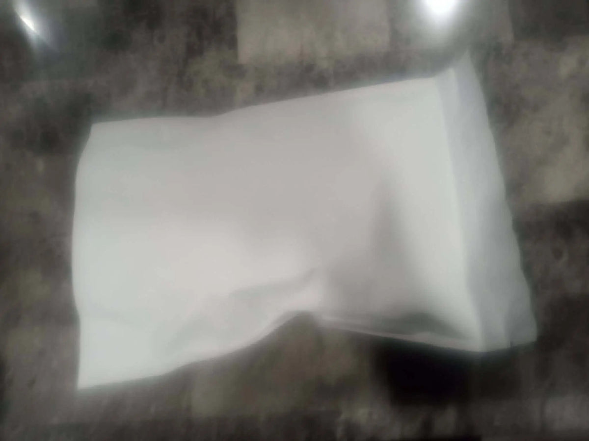A white slightly crumpled paper bag containing thca small buds flower quarter pound resting on a dark surface