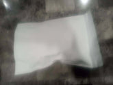 A white slightly crumpled paper bag containing thca small buds flower quarter pound resting on a dark surface